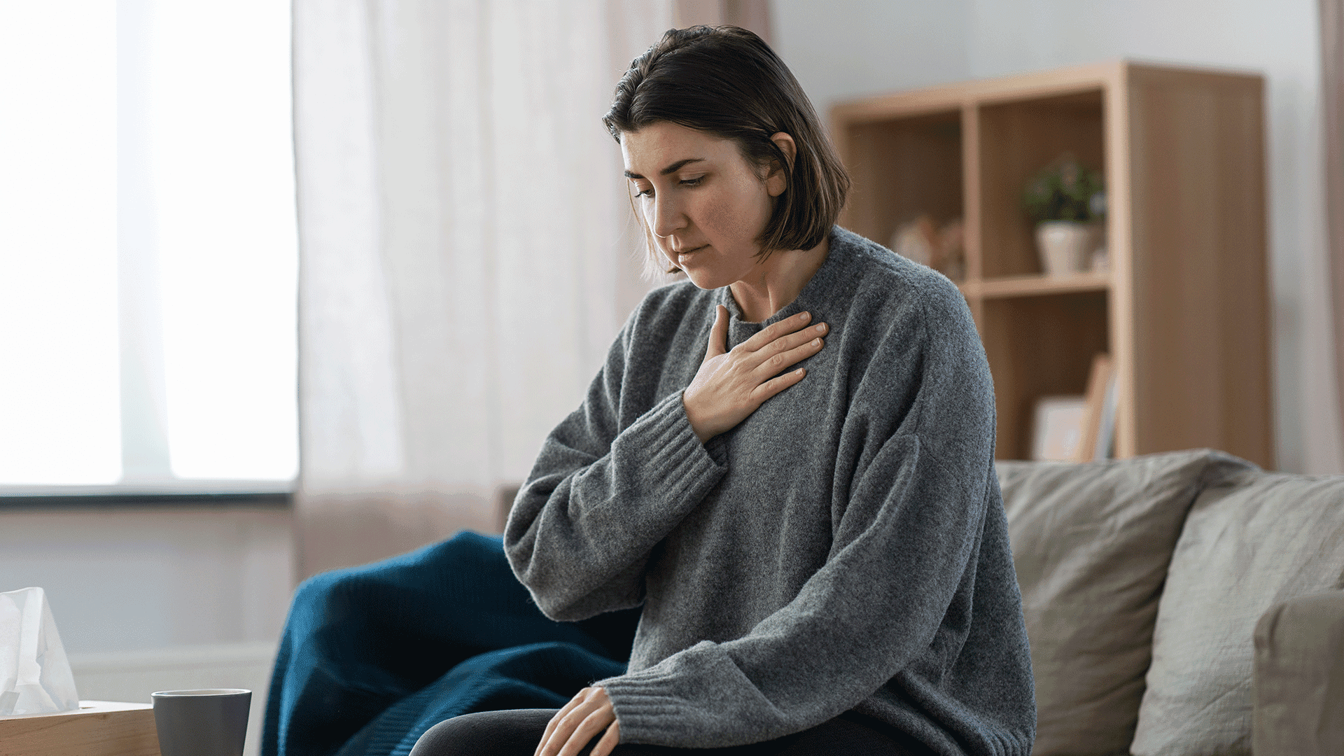 Woman sitting on the sofa and holding her right hand to the chest